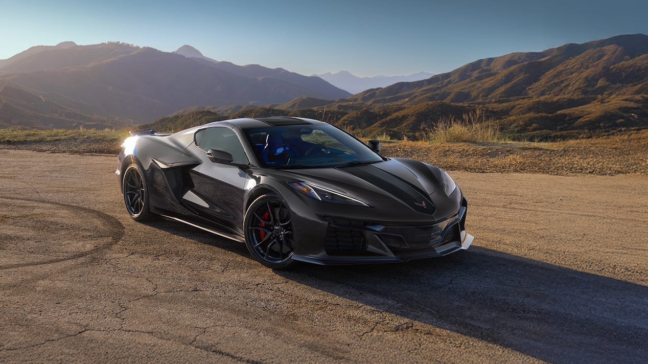 A Chevrolet Corvette Grand Sport X Is Parked on a Sunlit Road With Rolling Hills and Mountains in the Background at Golden Hour.