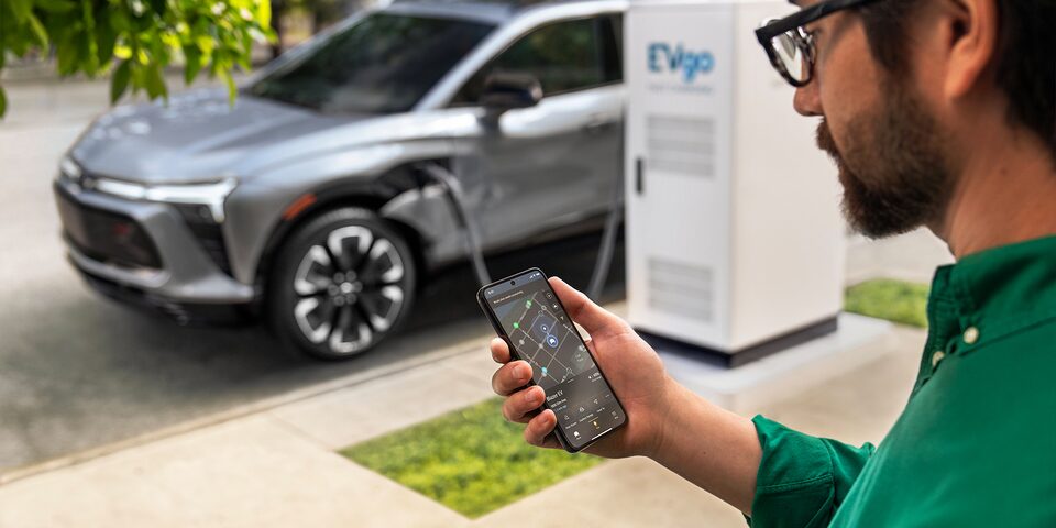 Una persona utiliza su teléfono móvil junto a una Blazer EV que está cargándose