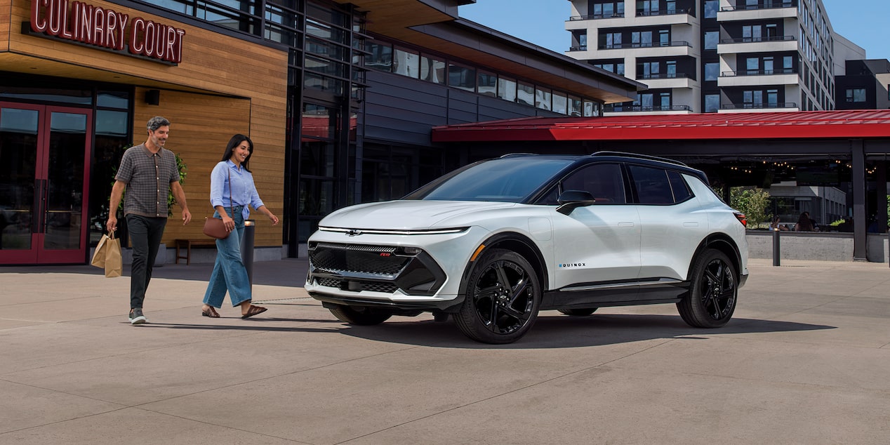 A Woman and Man Walking to 2024 Equinox EV Parked Outside of Store