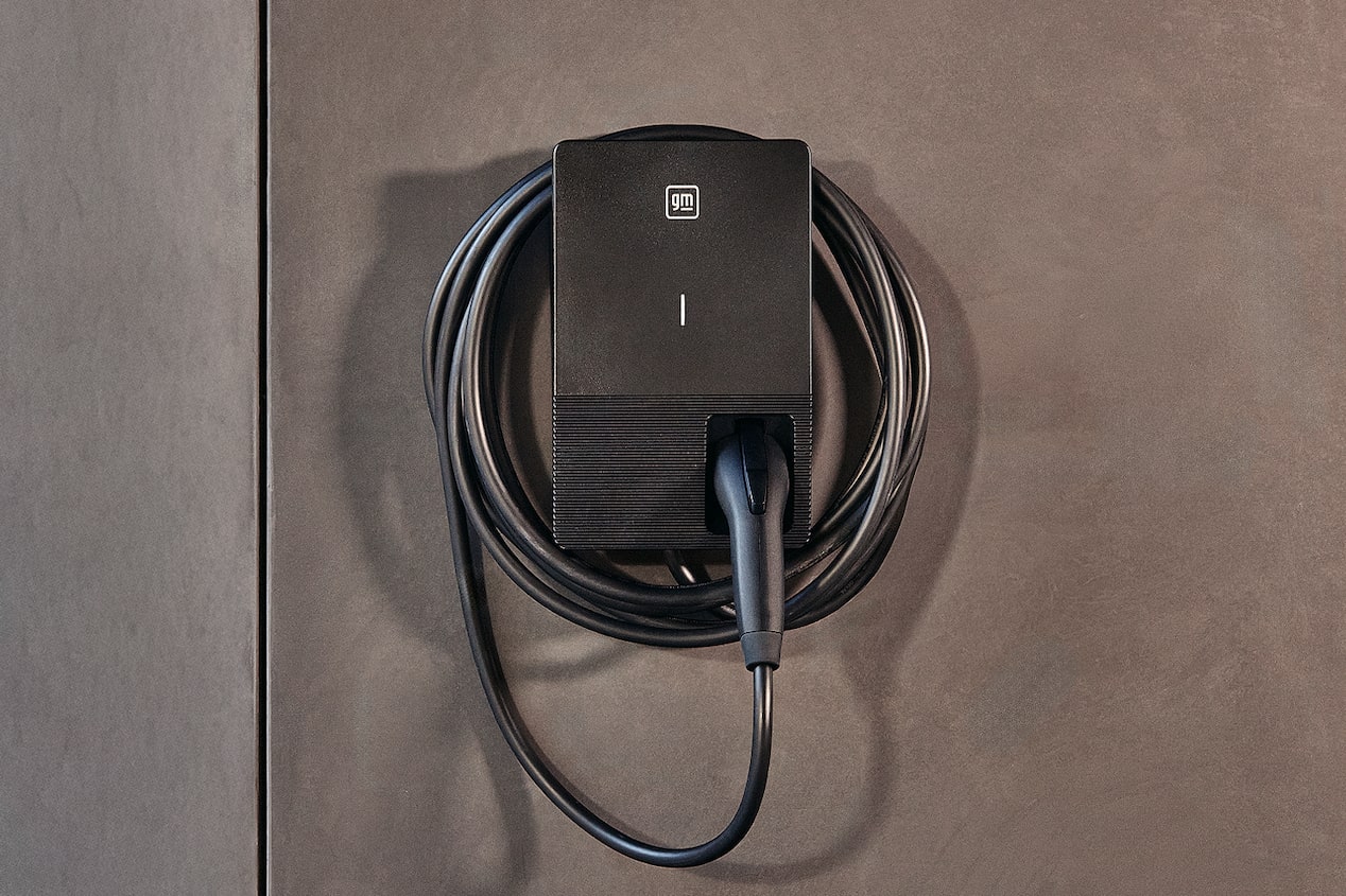 A Wall-Mounted GM PowerUp 2 Charger With a Coiled Charging Cable Secured Neatly Against a Smooth Gray Exterior Surface.