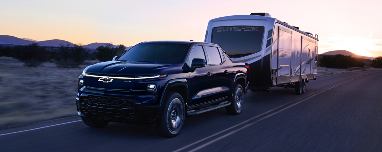 Front 3/4 Shot of Silverado EV Driving on Road at Dusk, Pulling Trailer