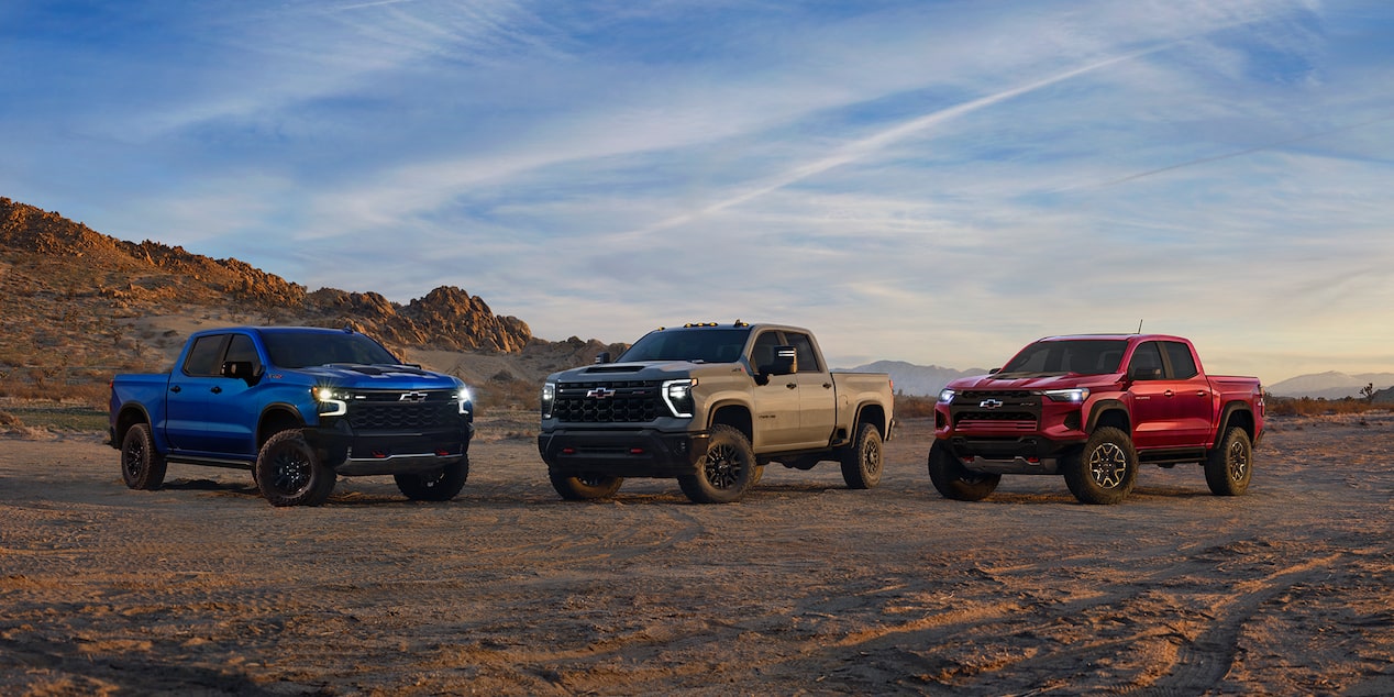2024 red Chevy Colorado, gray Silverado, and Silverado HD parked in the desert