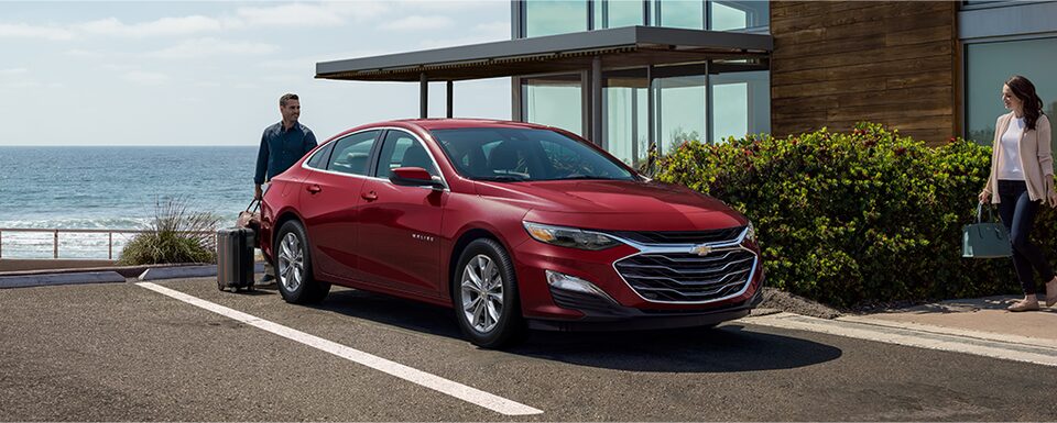 A Man Loads His Luggage Into The Chevy Malibu as It Sits Near the Ocean