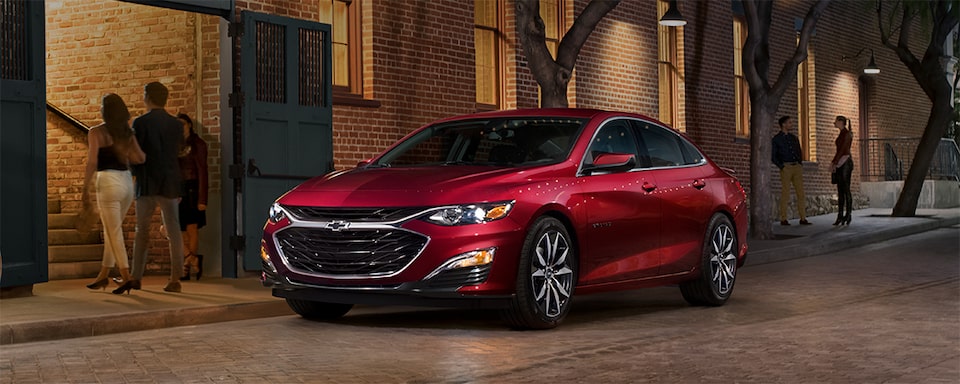 A Couple Leaves Their Radiant Red Tintcoat 2023 Chevy Malibu Parked in the City Center at Night 