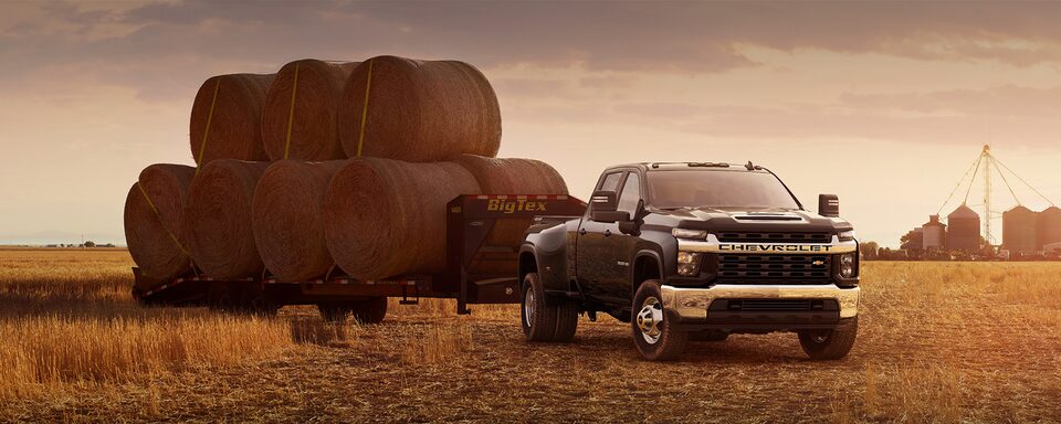 Navy Blue Commercial Chevy Silverado HD Towing Numerous Round Bales of Hay on a Farm