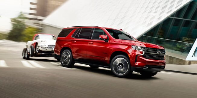 The Radiant Red Tintcoat 2023 Tahoe Turning a Corner while Hauling Another Car