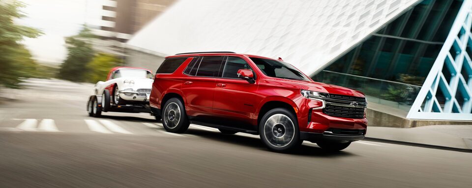 The Radiant Red Tintcoat 2023 Tahoe Turning a Corner while Hauling Another Car