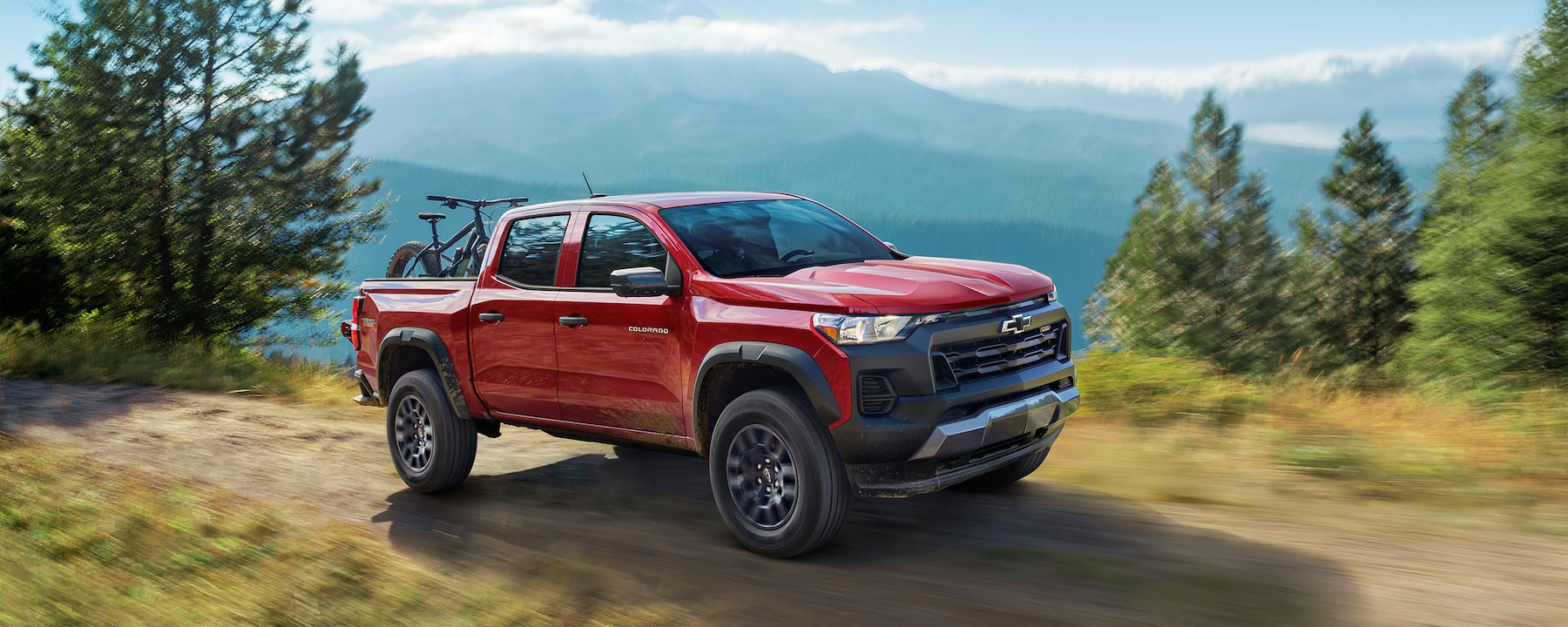 Red 2023 Chevy Colorado driving on mountain road carrying bike