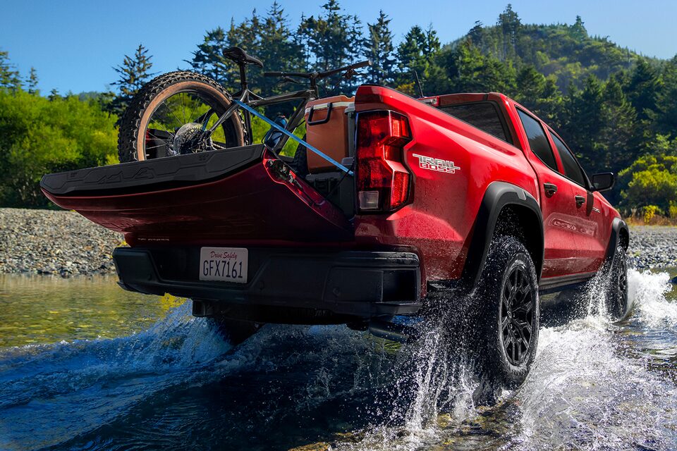 The Colorado Driving through A Small Body of Water with a Mountain Back Loaded in the Truck Bed