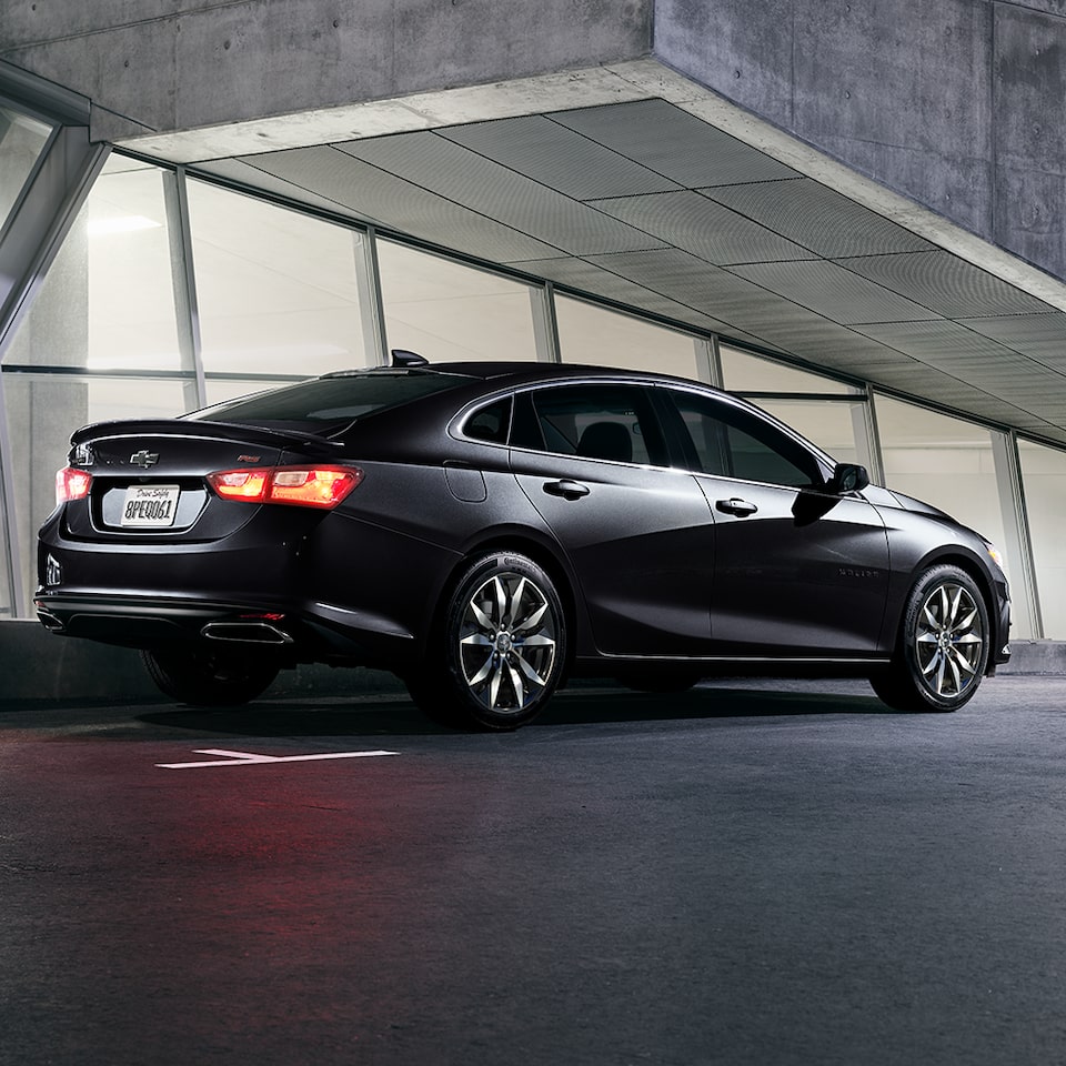 Three-Quarters View Of The 2024 Chevy Malibu In Mosaic Black Metallic With Tail Lamps On