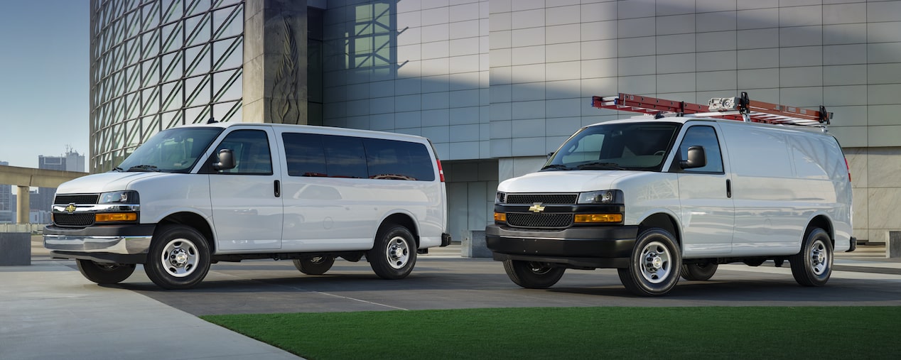 2025 Chevy Commercial Express Vans Parked Outside Glass Office Building
