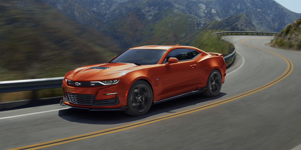 A Vivid Orange Metallic 2024 Chevy Camaro Driving Around Bend On A Scenic Road