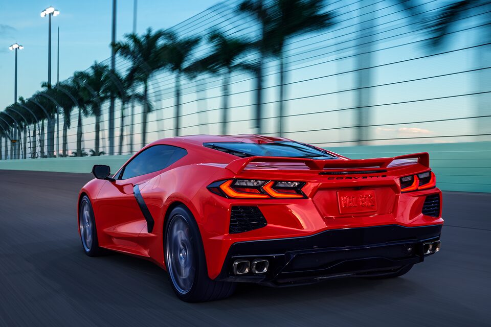 Torch Red 2024 Corvette Driving On Race Track At Dusk with Palm Trees Lining the Track