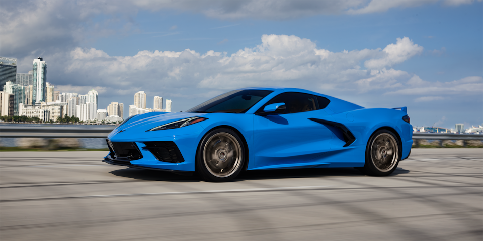 Rapid Blue 2024 Chevy Corvette Stingray Driving Down a Highway with a Cityscape Background
