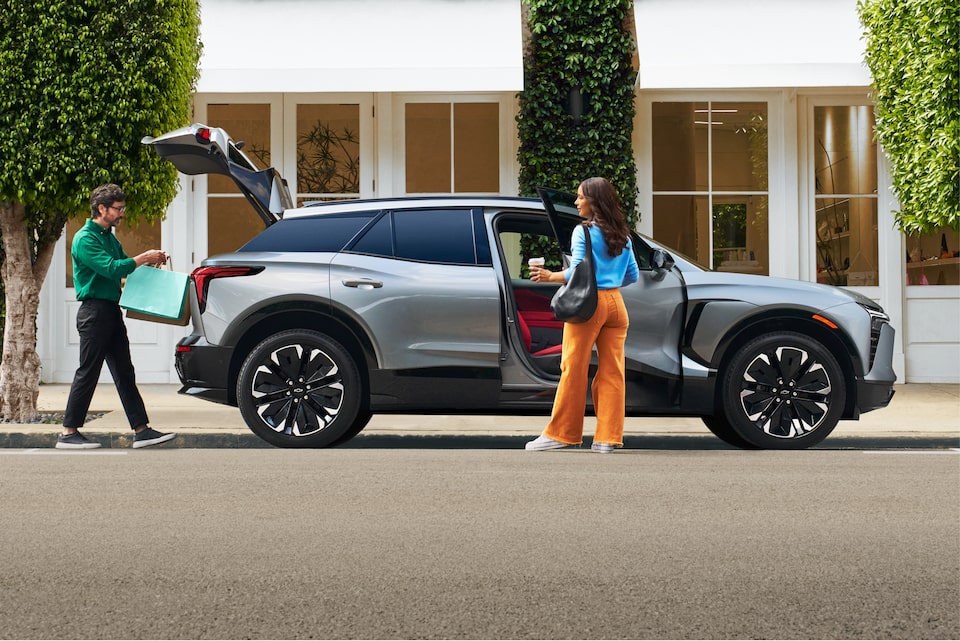 Man Loads Bag into Trunk of Blazer EV while Woman Boards Passenger Seat, Coffee in Hand