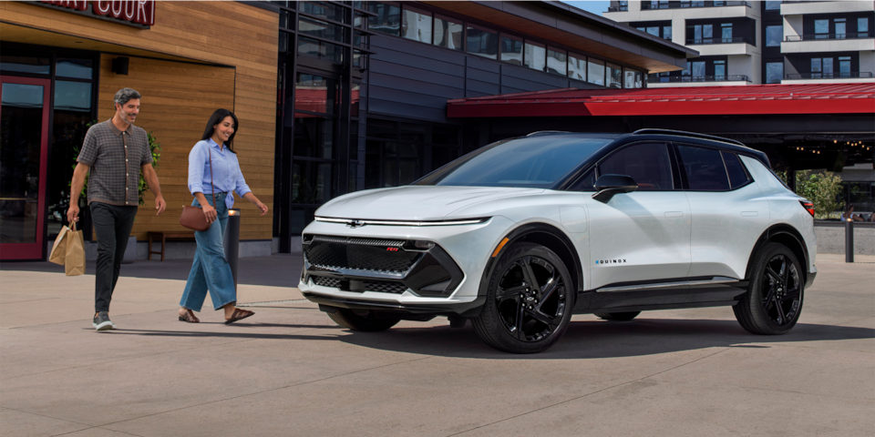 Un hombre y una mujer caminando hacia una Chevy Equinox EV 2024 estacionada en la ciudad