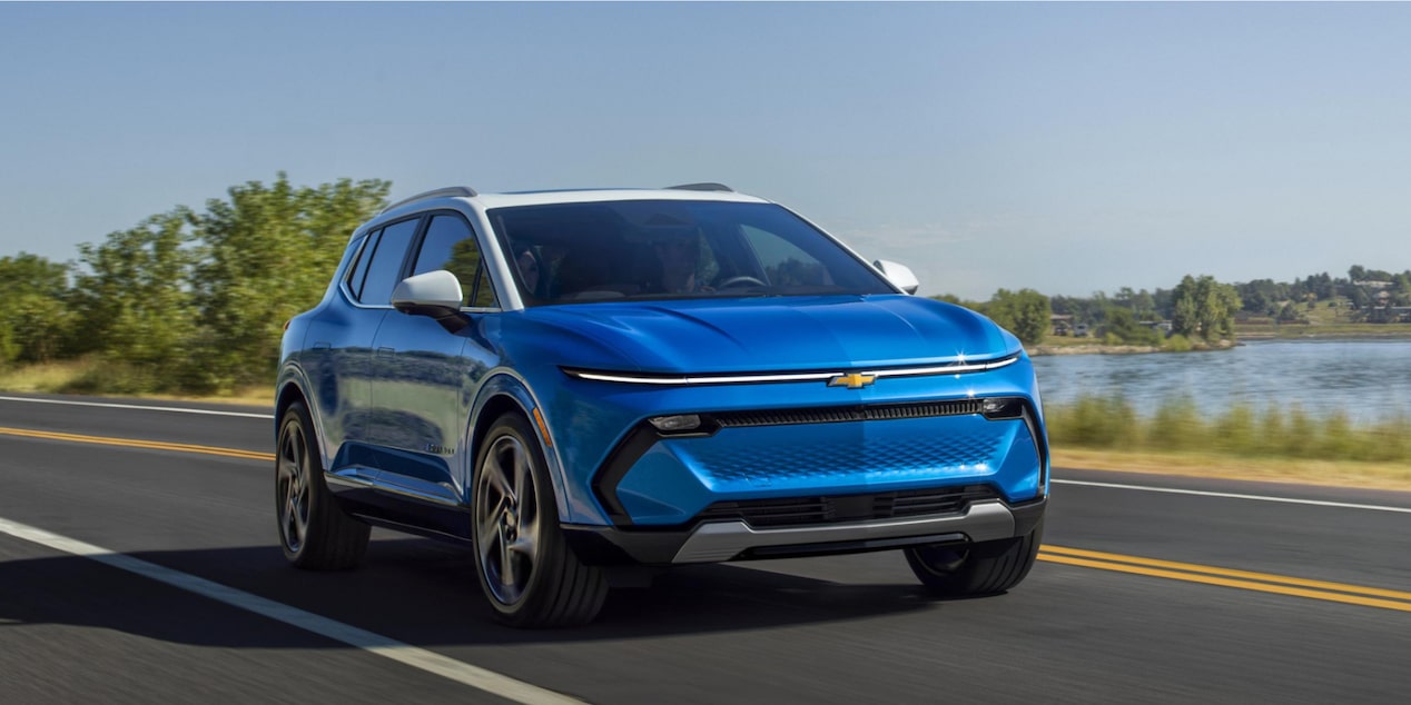 a blue suv driving on a paved road next to water