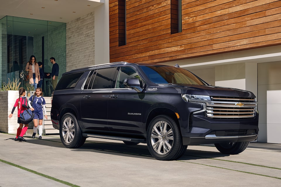 The Midnight Blue Metallic MY24 Chevy Suburban Parked In-Front of a Modern Home with two children 