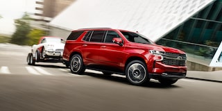 The Radiant Red Tintcoat 2024 Tahoe Turning a Corner while Hauling Another Car