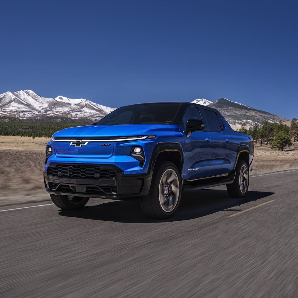 Three-Quarters View Of The Front End Of The 2024 Silverado EV Driving In Forest