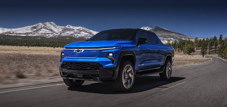 2024 Chevy Silverado EV Driving Down A Road With Mountains In The Background