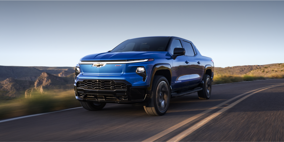 The 2024 Chevy Silverado EV Cruising Down A Scenic Road With Mountains