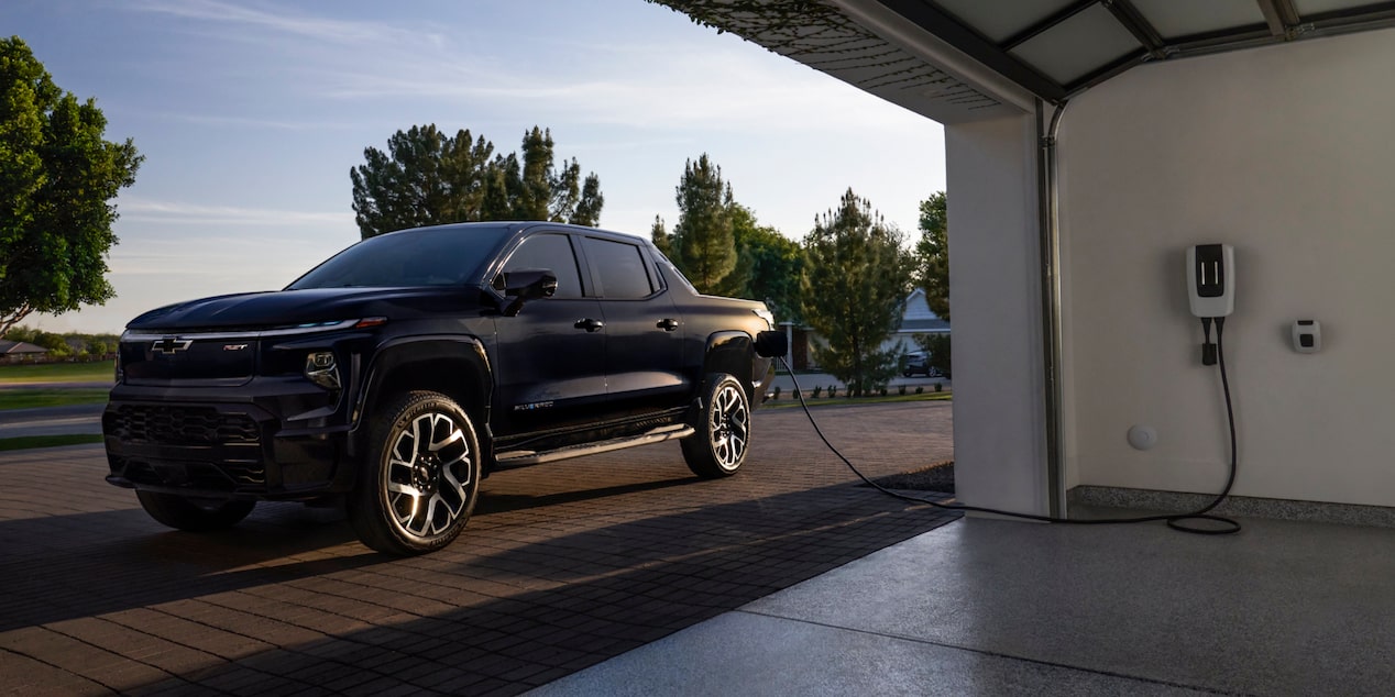 Una Chevy Silverado EV 2024 estacionada fuera de un garaje, enchufada a un puerto de carga