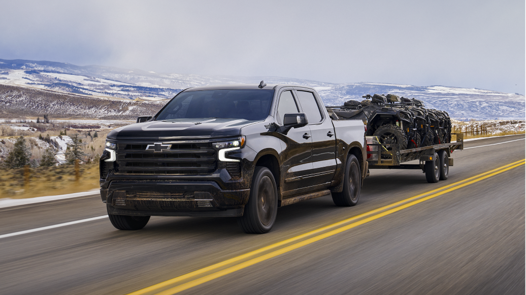 Black Silverado towing 4 full sized ATV's on a trailer on the highway