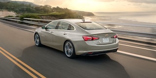 Vista trasera de una Chevy Malibu 2025 color Gris Mineral circulando junto a la orilla del mar