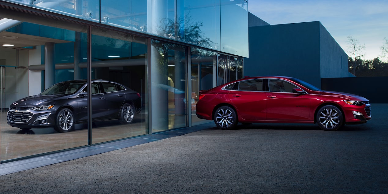 A Red 2025 Chevy Malibu Parked outside and Another Black Chevy Malibu Parked Inside the Building