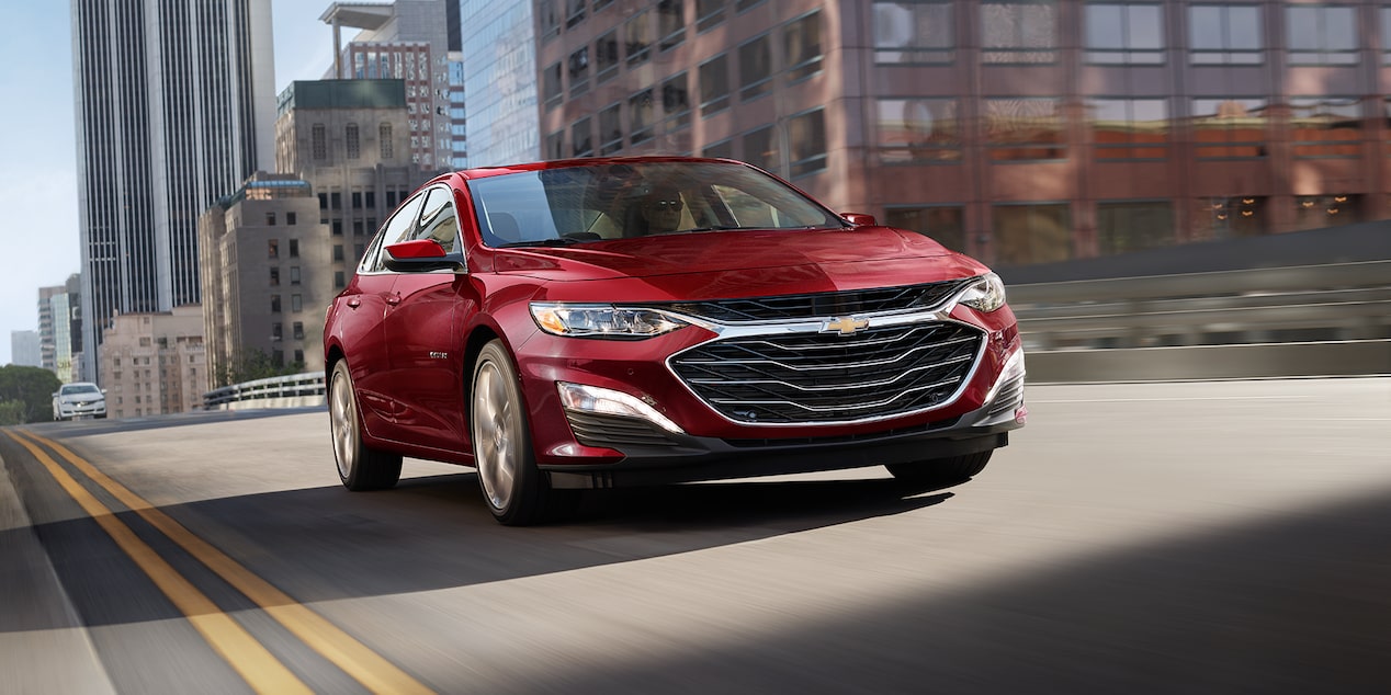Vista frontal desde abajo de una Chevy Malibu color Rojo circulando por la ciudad