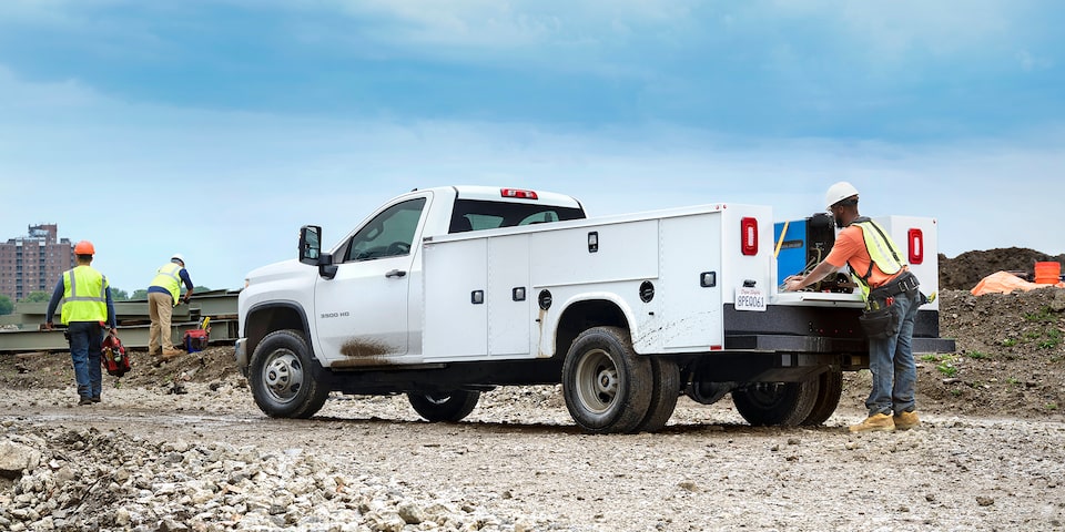 Un trabajador de la construcción guardando herramientas en la caja de uso general de una Chevy Silverado 3500 HD de chasis con cabina 2025