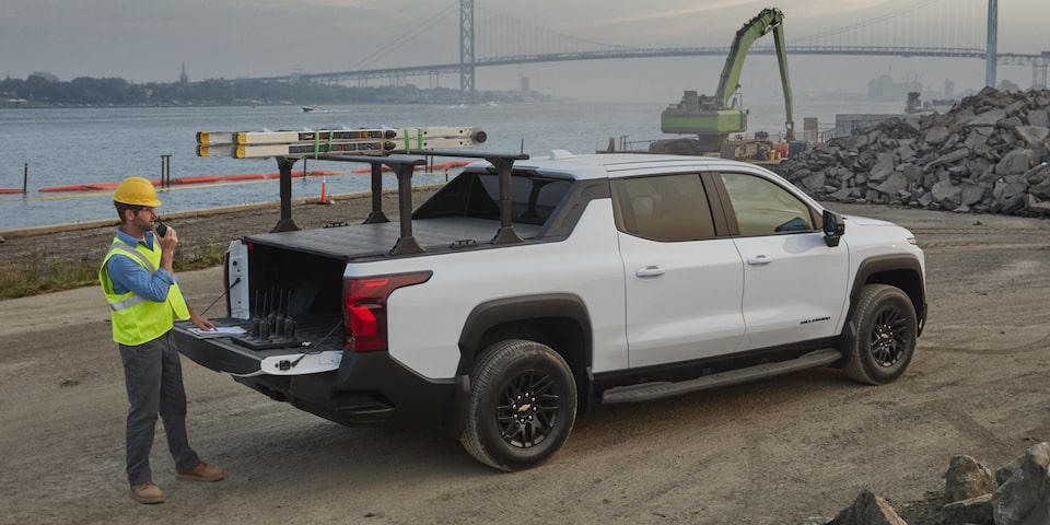 Vista trasera de medio perfil de una Silverado EV 2025 blanca con un hombre abriendo la cajuela