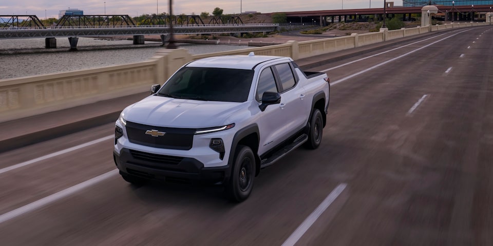 Vista de medio perfil de una Chevy Silverado EV circulando por un camino bajo un cielo del atardecer