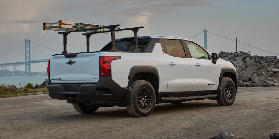 Vista trasera de medio perfil de una Chevy Silverado EV 2025 blanca circulando por un camino al atardecer