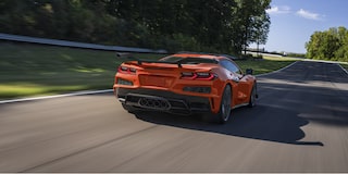 Three Quarters Rear View of an Orange Chevy Corvette Z06 Driving Down the Road on a Sunny Day