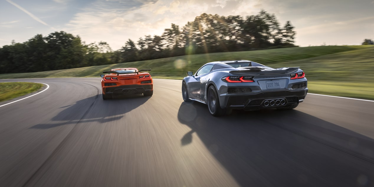 Two Orange and Silver Colored Chevy Corvette Z06s Racing Down the Road on a Sunny Day