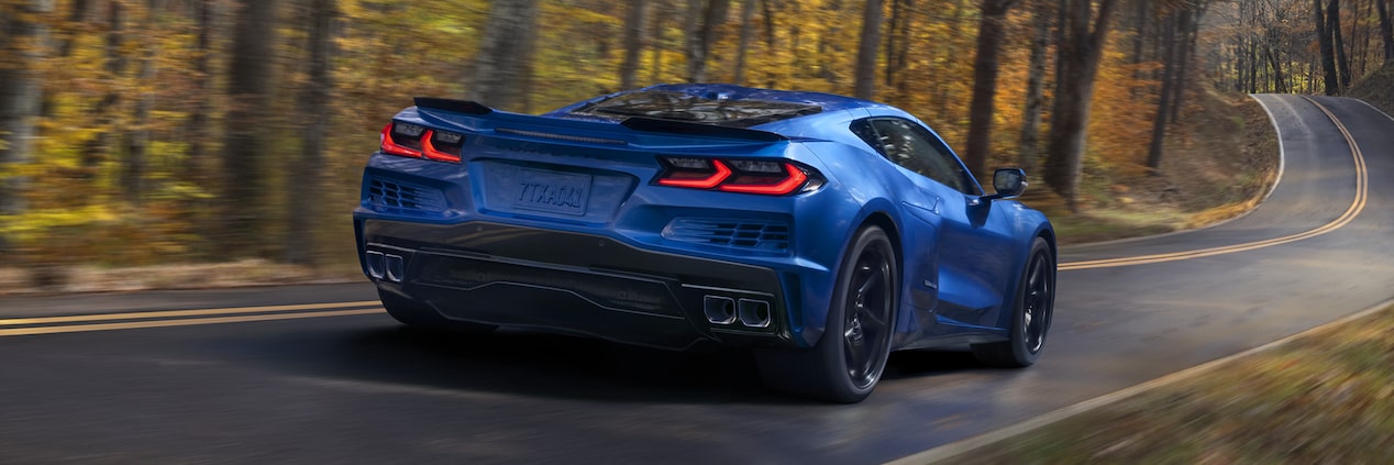 Vista trasera de medio perfil de un Chevy Corvette E-Ray en Azul circulando por un camino rodeado de árboles