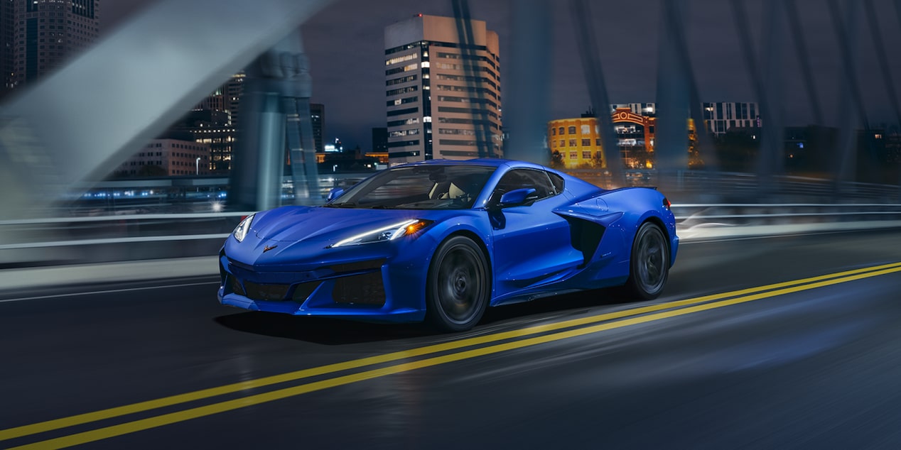 Three Quarters View of a 2025 Blue Chevy Corvette Driving Down the Bridge at Night