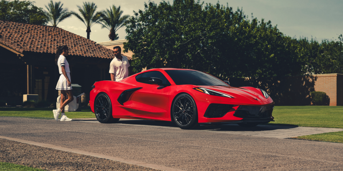 Three Quarters View of a Red 2025 Chevy Corvette Stingray with a Man and a Woman behind It