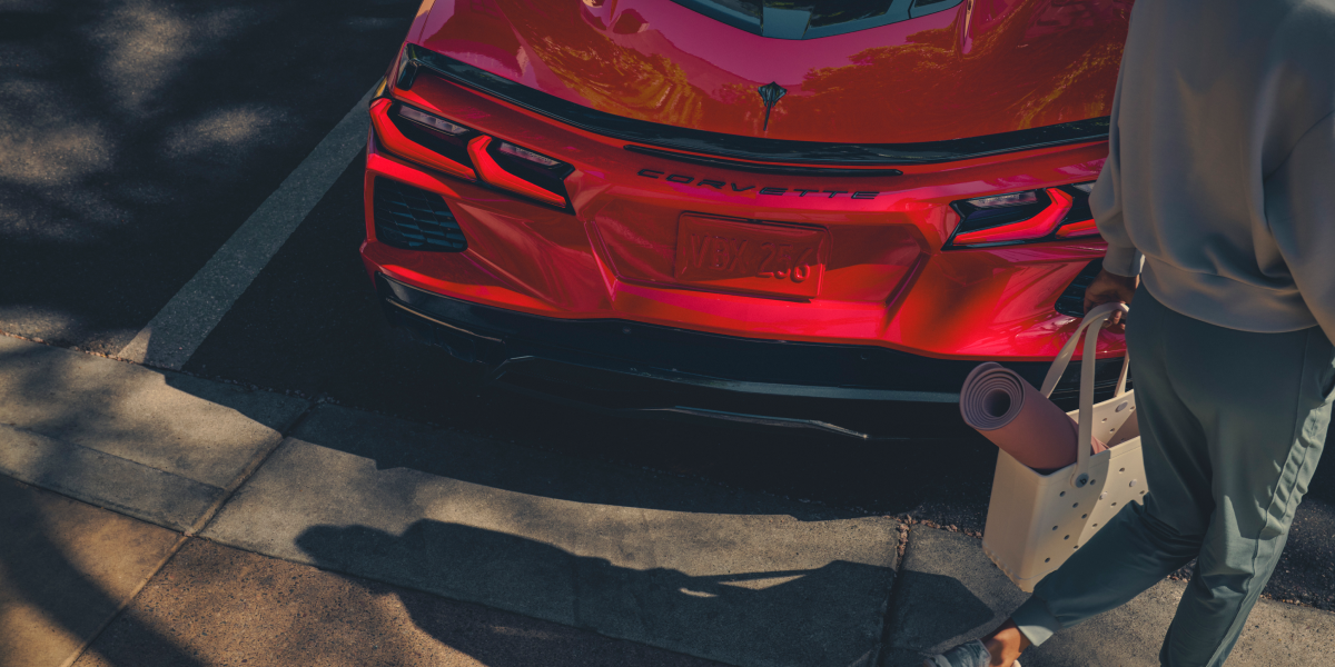 A Man with a Shopping Bag Walking Away from the Rear of a 2025 Red Chevy Corvette Stingray