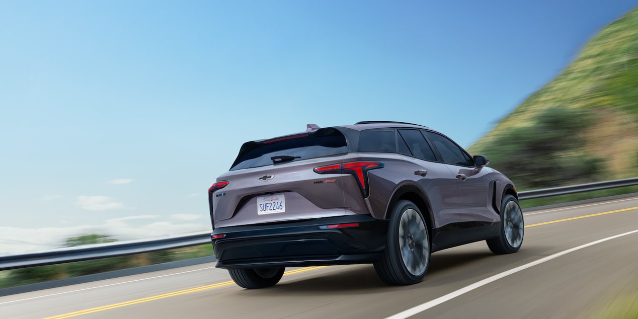 Rear Three Quarters View of a Gray 2025 Chevy Blazer EV Going down the Road under a Clear Blue Sky