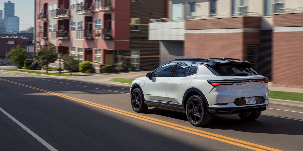 Three Quarters Rear View of a White 2025 Chevy Equinox EV Driving Down the Road