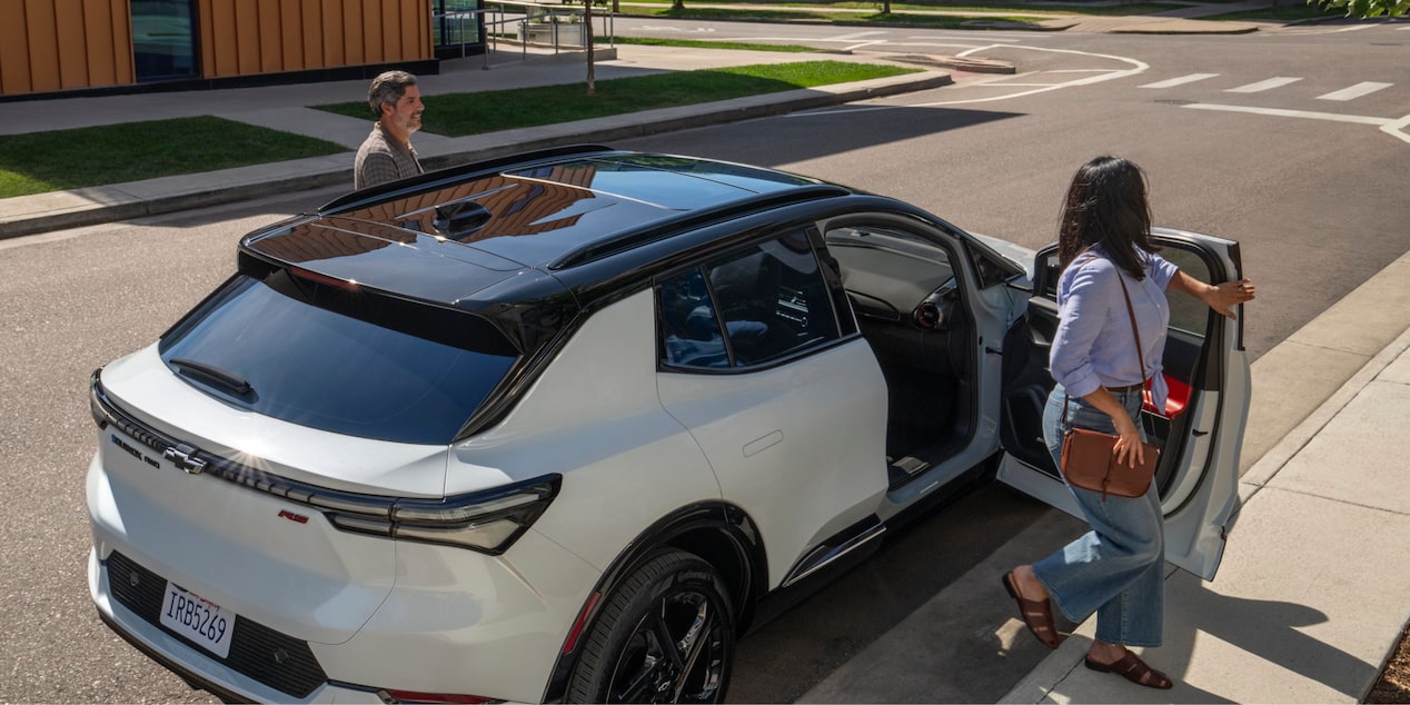 Three Quarters Rear View of a Black and White 2025 Chevy Equinox EV with a Woman Closing Its Door