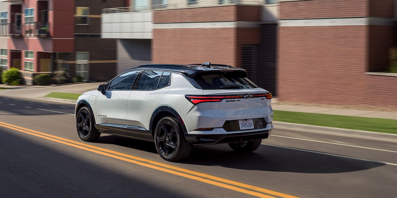 Three Quarters Rear View of a White 2025 Chevy Equinox EV Driving Down the Road