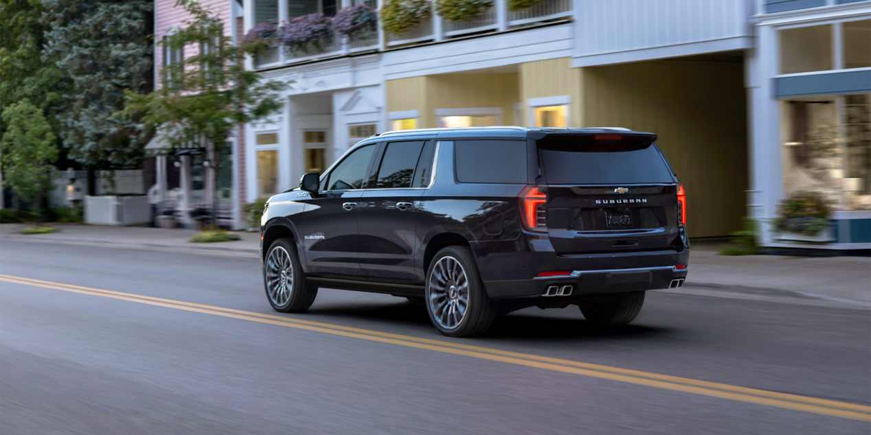 Rear Three-Quarters View of the 2025 Chevrolet Suburban SUV Driving Through Downtown