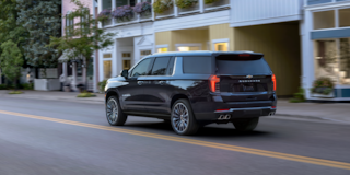 Rear Three-Quarters View of the 2025 Chevrolet Suburban SUV Driving Through Downtown