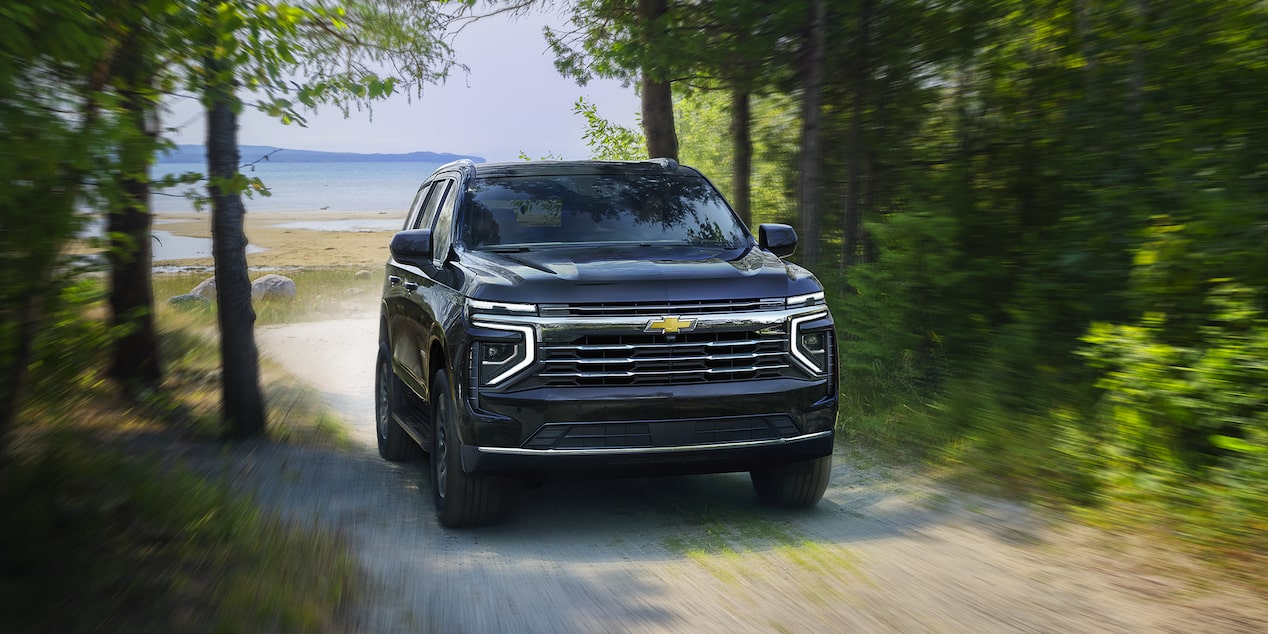 Una Chevy Tahoe 2025 andando por un camino de grava cerca de un lago