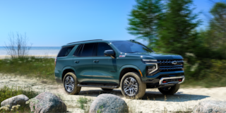 Vista lateral de SUV Chevrolet Tahoe 2025 circulando por una playa arenosa, al lado de un lago