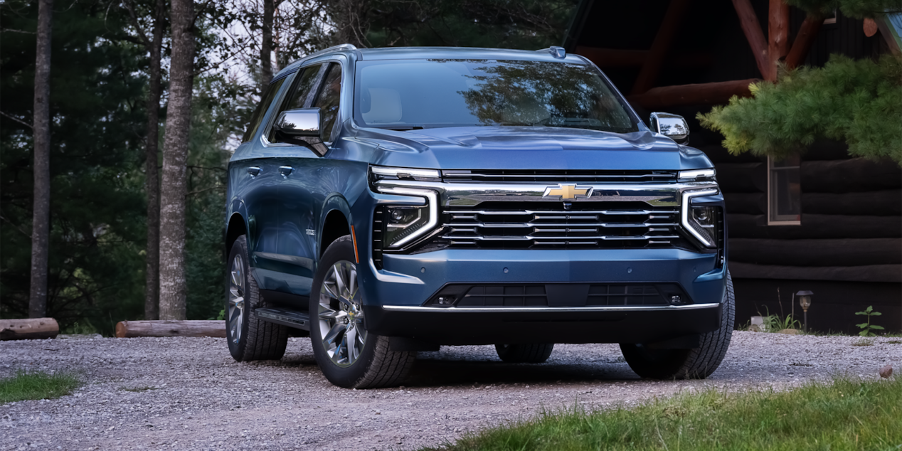 Vista delantera de medio perfil de Chevrolet Tahoe 2025 estacionado en frente de una cabaña en el bosque